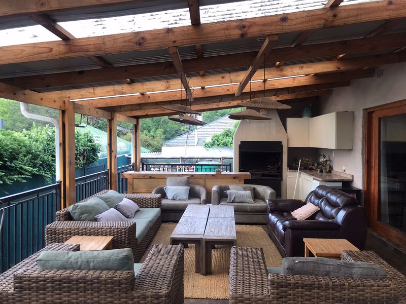 Covered outdoor patio featuring a timber pergola roof, built-in braai, and integrated cabinetry, providing a functional space for outdoor entertaining.