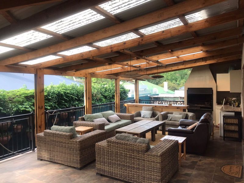 Spacious covered patio featuring a timber pergola with translucent roofing, built-in braai, and tiled flooring, ideal for outdoor entertaining.