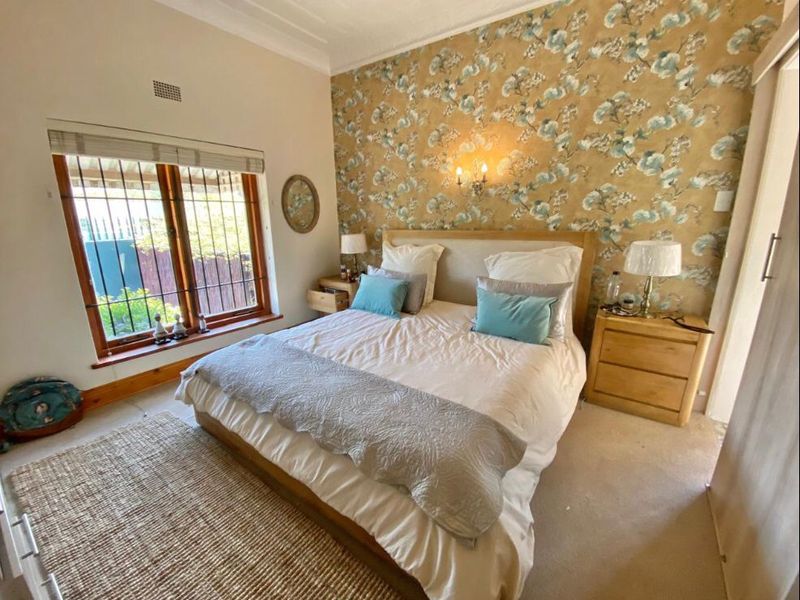 A cozy bedroom featuring a decorative floral feature wall, built-in wardrobe, and security bars on the window.