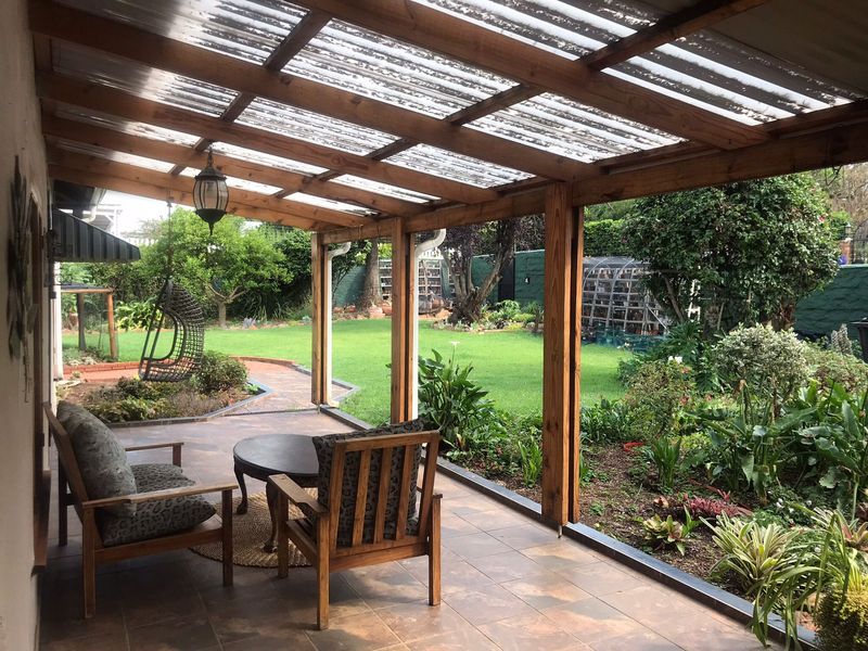 A covered patio featuring a timber pergola with a corrugated roof, tiled flooring, and direct access to a landscaped garden.
