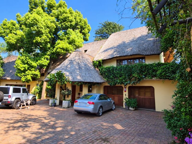 Front elevation of a charming thatched-roof property featuring a spacious brick-paved driveway and integrated double garage.