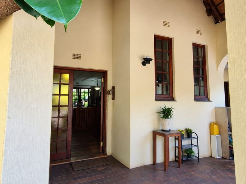 A covered patio area featuring brick paving, timber-framed windows, and a glass-paneled entrance door leading into the home.