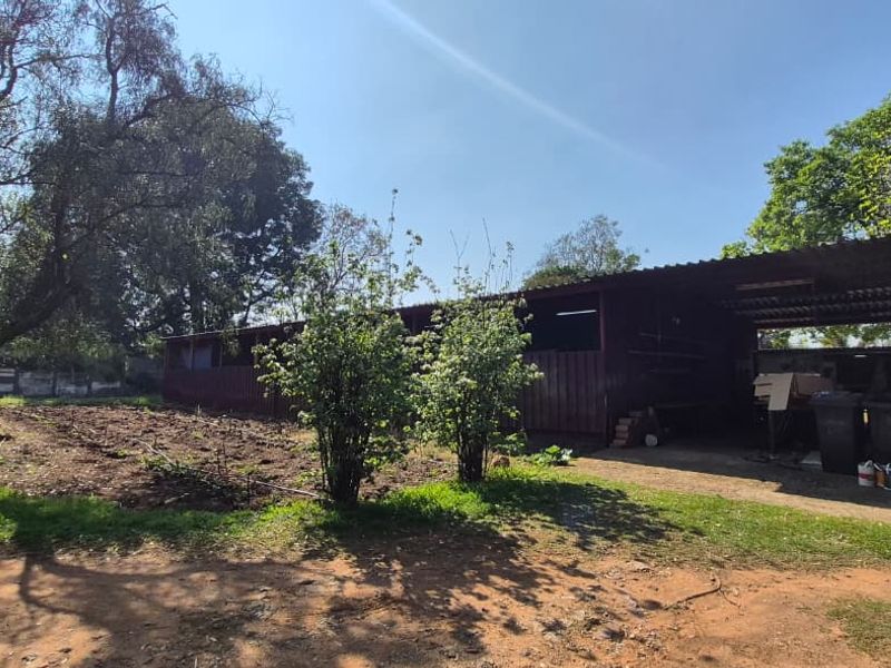 An exterior view of a rustic, open-sided outbuilding or stable structure situated on a small holding with surrounding garden space.