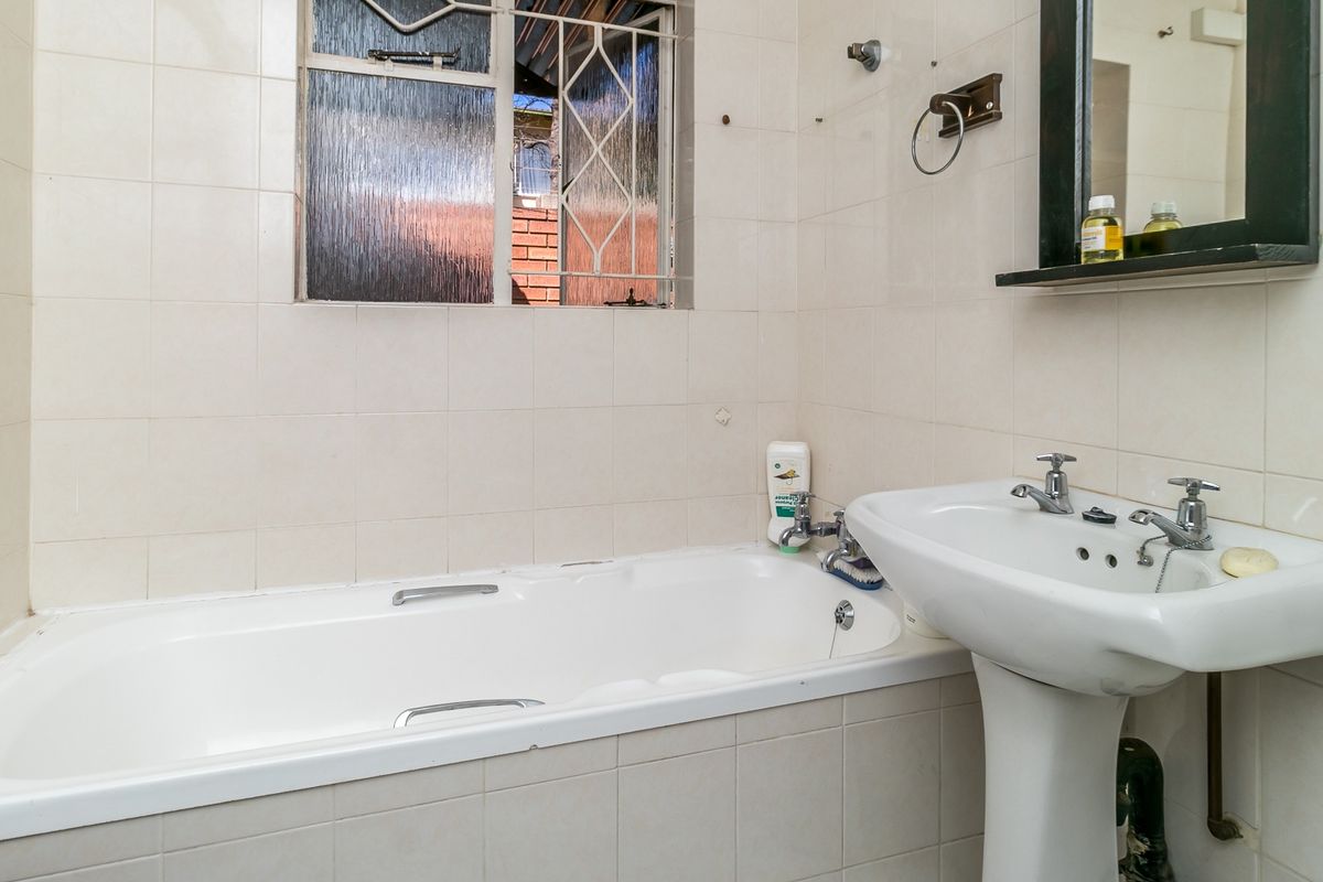 A functional bathroom featuring a pedestal basin, built-in bathtub, and tiled walls, offering a blank canvas for modern renovation and aesthetic updates.