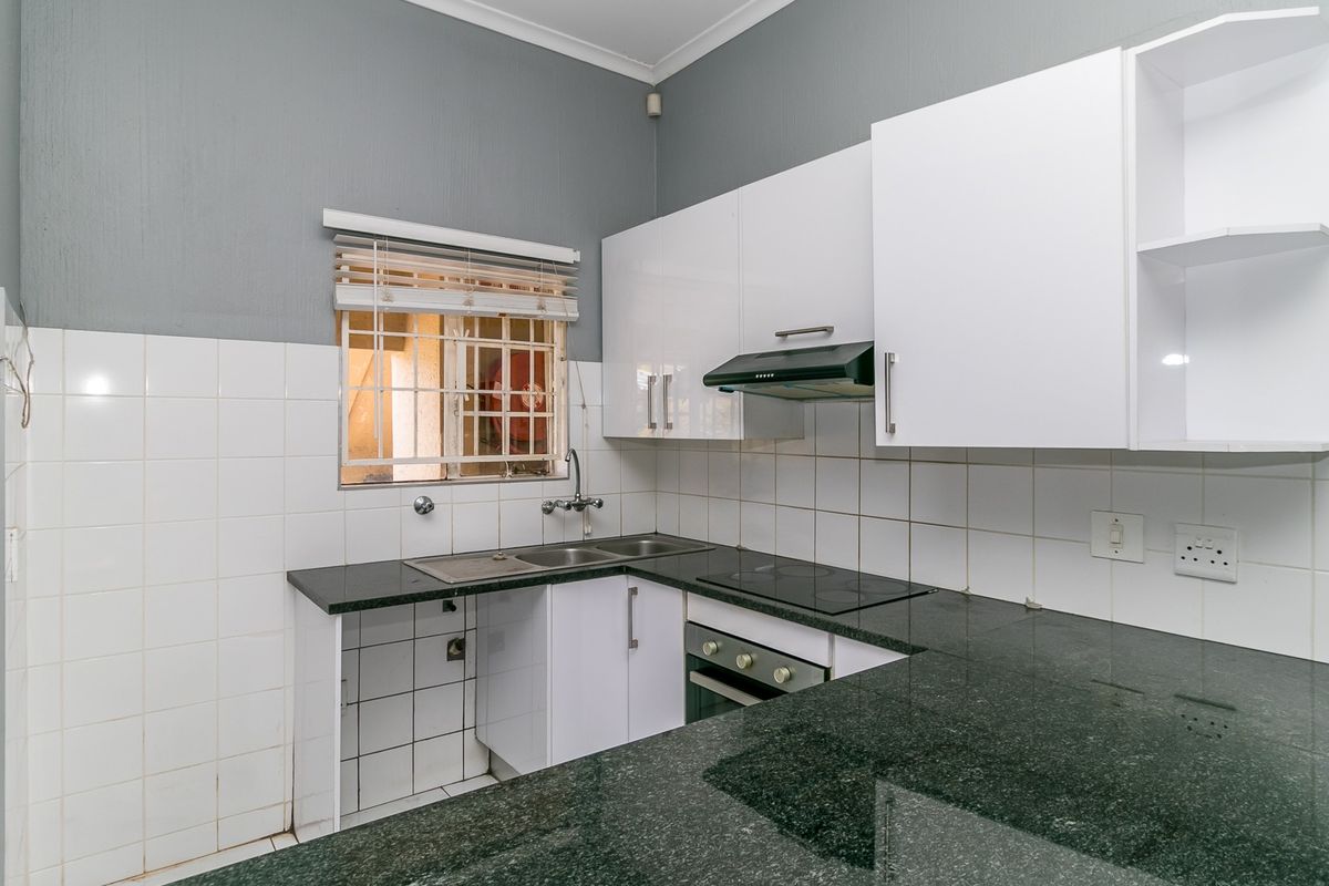 A functional kitchen featuring granite countertops, white cabinetry, built-in oven, electric hob, extractor fan, and a tiled backsplash.