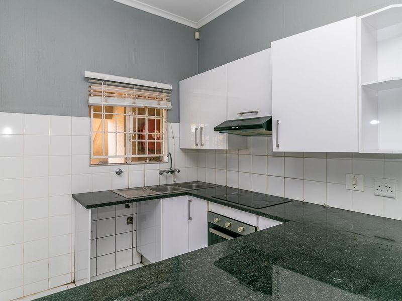 A functional kitchen featuring granite countertops, white cabinetry, built-in oven, electric hob, extractor fan, and a tiled backsplash.