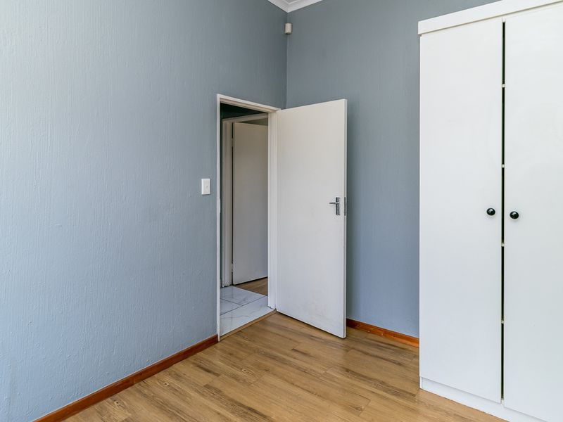 A clean, empty bedroom featuring light blue walls, wood-look laminate flooring, and a built-in white wardrobe.