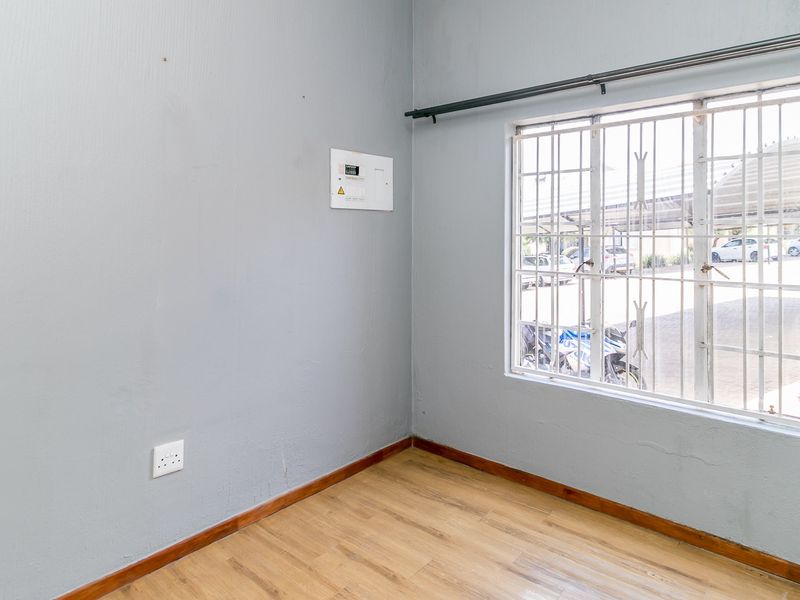 An empty bedroom featuring laminate flooring, a window with security bars, and a wall-mounted electrical distribution board.