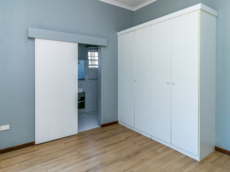 A clean, empty bedroom featuring laminate flooring, a large built-in wardrobe, and a sliding door leading to an en-suite bathroom.