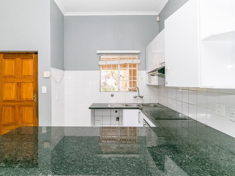 A functional kitchen featuring granite countertops, built-in cabinetry, an electric hob, and a tiled backsplash, offering a clean and practical workspace.