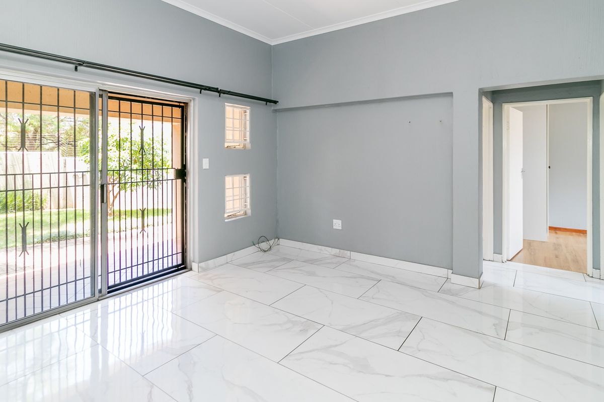 An empty living room featuring modern marble-look floor tiles, grey walls, and a sliding glass door with a security gate leading to the garden.
