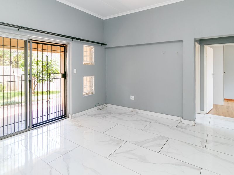 An empty living room featuring modern marble-look floor tiles, grey walls, and a sliding glass door with a security gate leading to the garden.