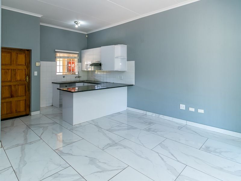 An open-plan living area featuring modern marble-look tiled flooring, a compact kitchen with granite countertops, and white cabinetry.