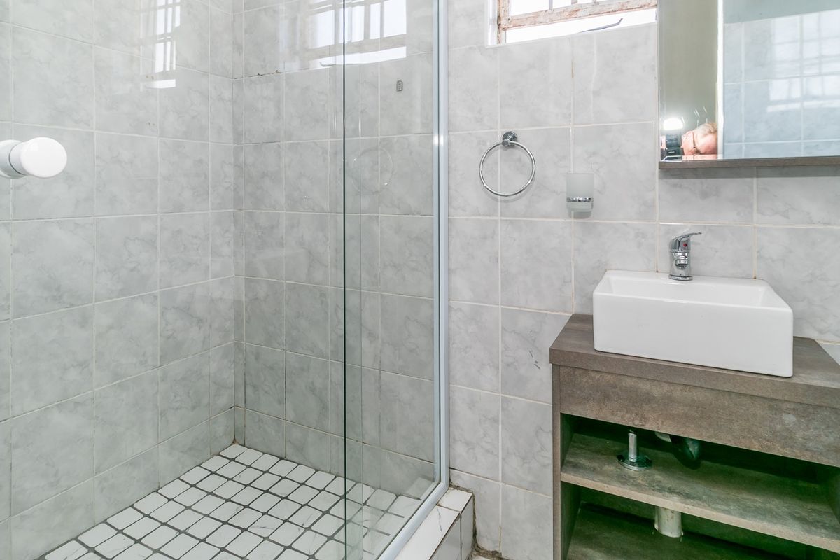 A functional bathroom featuring a glass-enclosed shower, a modern vessel sink set on a vanity cabinet, and neutral wall tiling.