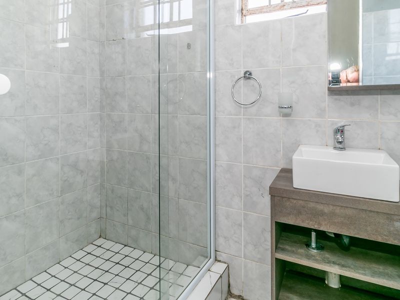 A functional bathroom featuring a glass-enclosed shower, a modern vessel sink set on a vanity cabinet, and neutral wall tiling.