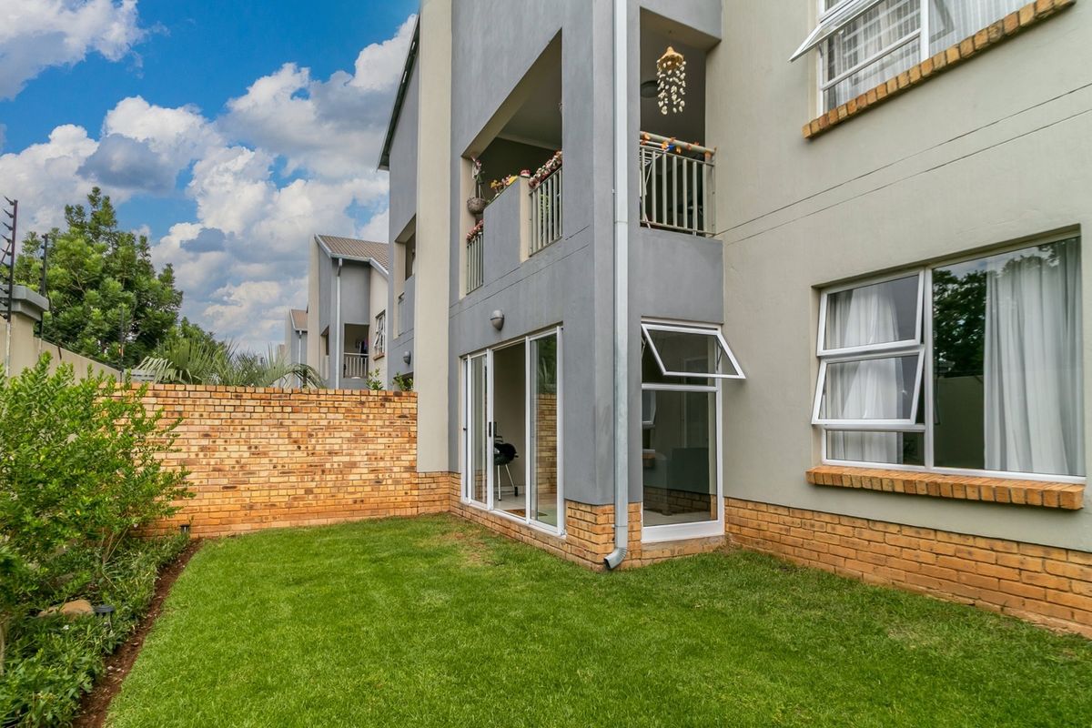 Rear view of the apartment building featuring a private garden, brick boundary wall with electric fencing, and a balcony with sliding door access.