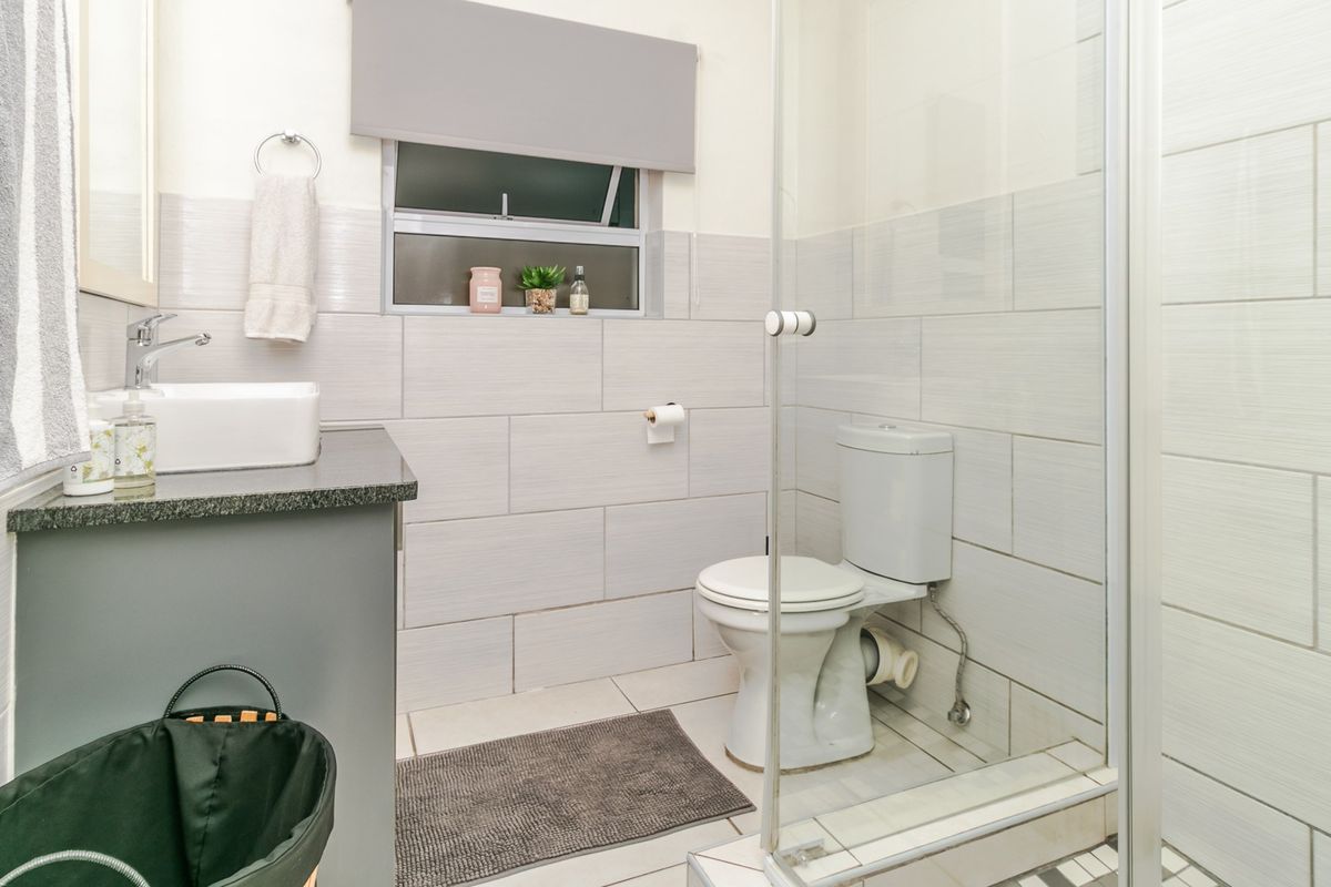 A modern bathroom featuring a vessel sink on a granite vanity, a glass-enclosed shower, and neutral wall tiling.