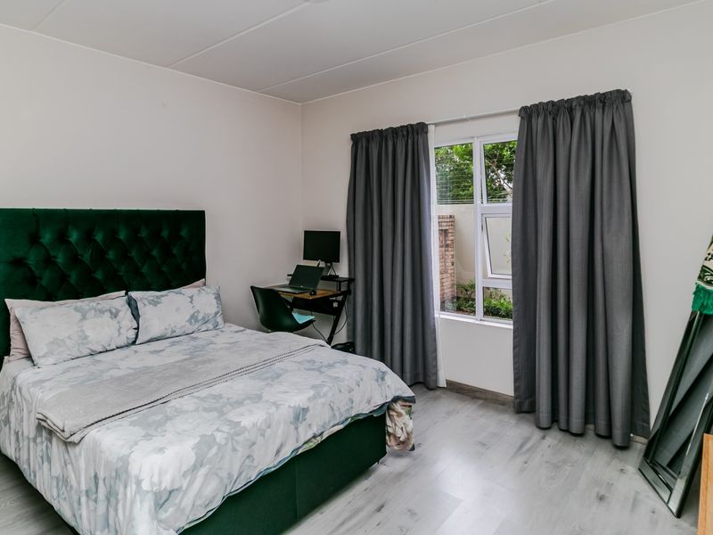 A well-maintained bedroom featuring light-toned laminate flooring, neutral walls, and a window with curtain tracks.