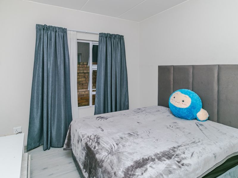 A bedroom featuring laminate flooring and a window with curtains, providing a functional space for rest.