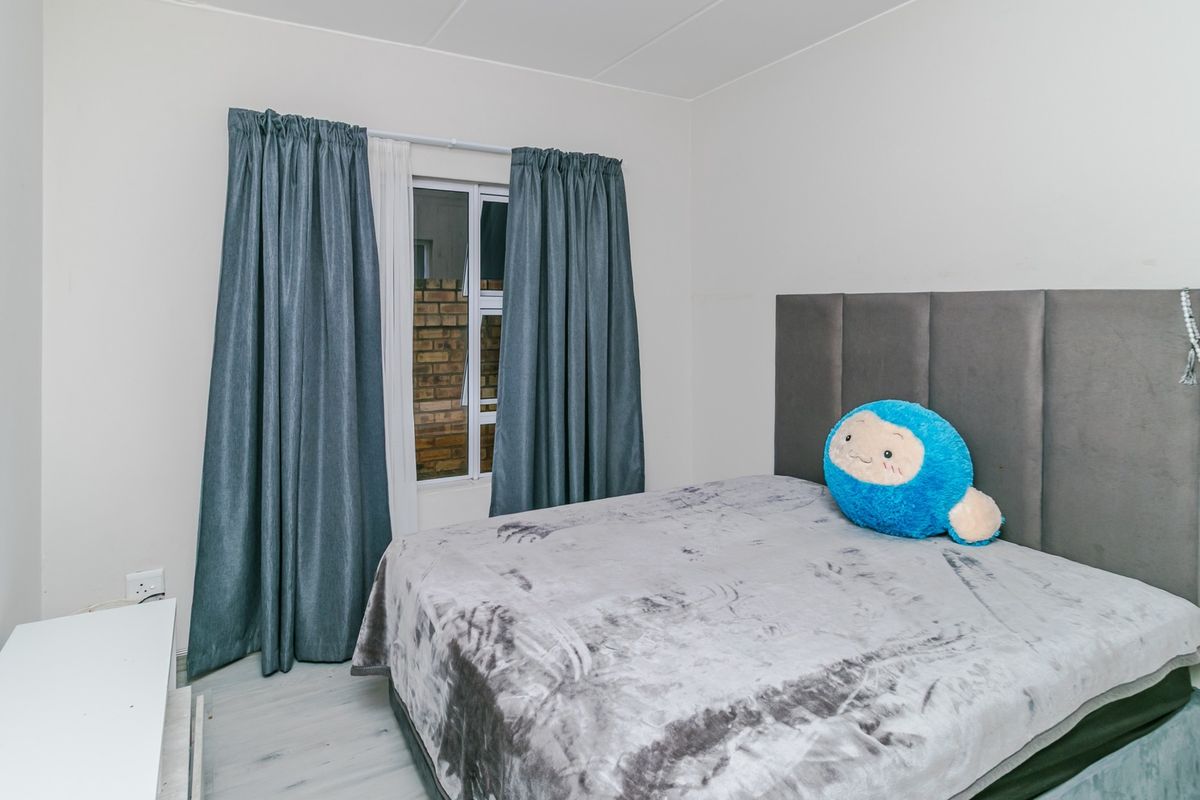 A bedroom featuring laminate flooring and a window with curtains, providing a functional space for rest.