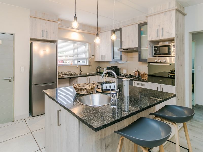 Modern kitchen featuring a central island with granite countertops, built-in oven, microwave, and ample cabinetry, finished with neutral tiled flooring.