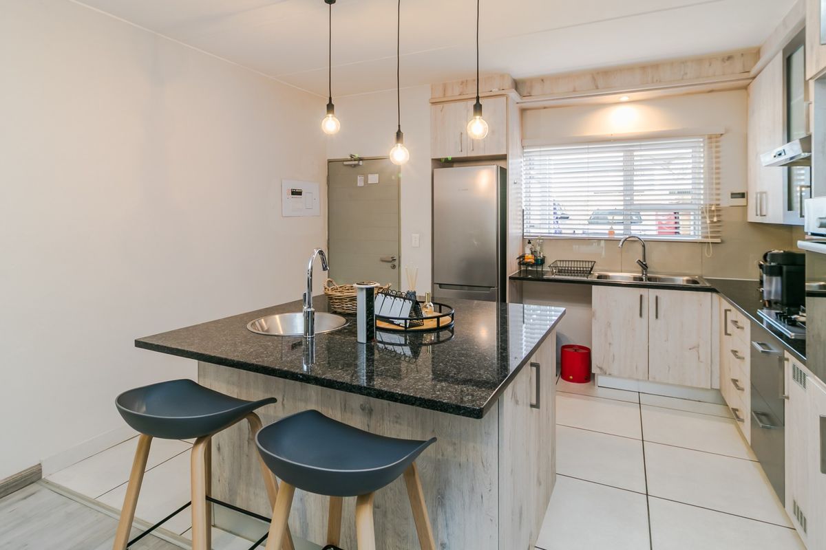 Modern kitchen featuring a central island with granite countertops, built-in oven, extractor fan, and ample cabinetry, complemented by tiled flooring and pendant lighting.