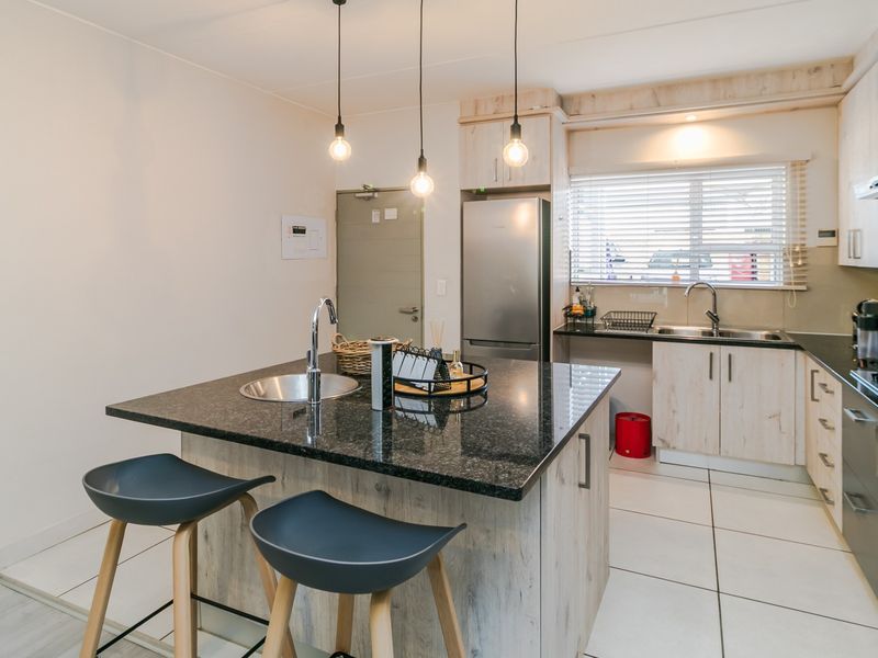 Modern kitchen featuring a central island with granite countertops, built-in oven, extractor fan, and ample cabinetry, complemented by tiled flooring and pendant lighting.