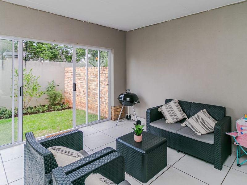 A covered patio area featuring tiled flooring and large sliding glass doors that open onto a private garden with a brick boundary wall.
