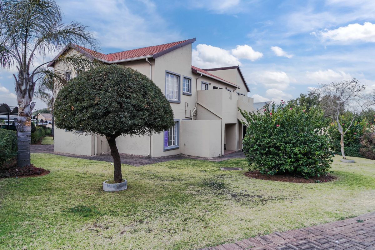 Rear view of a multi-story apartment building featuring a tiled roof, exterior staircase, and balcony, set within a landscaped garden area.