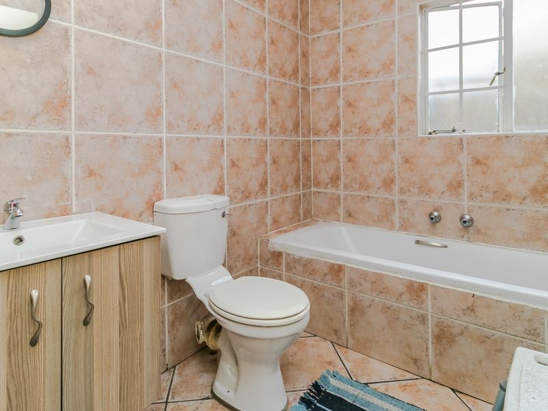 A functional bathroom featuring a built-in vanity, toilet, and bathtub with dated ceramic wall and floor tiling.