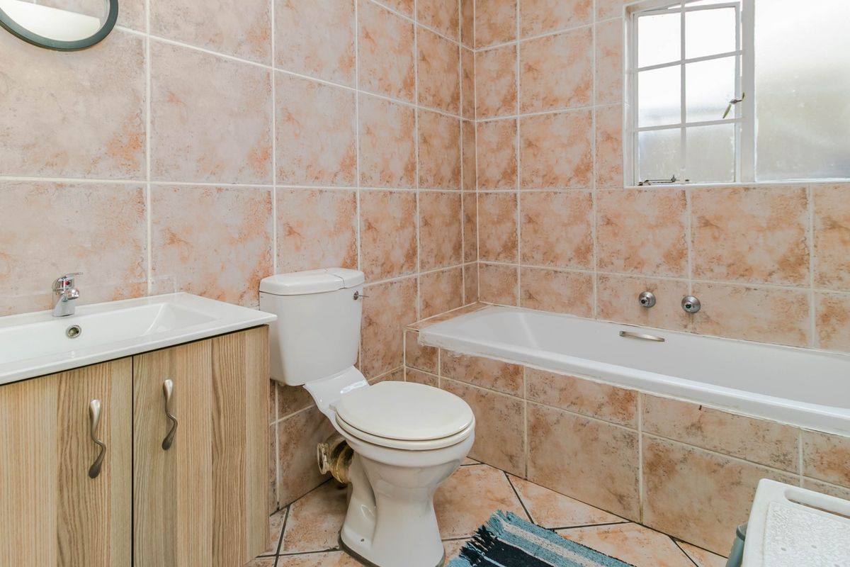 A functional bathroom featuring a built-in vanity, toilet, and bathtub with dated ceramic wall and floor tiling.