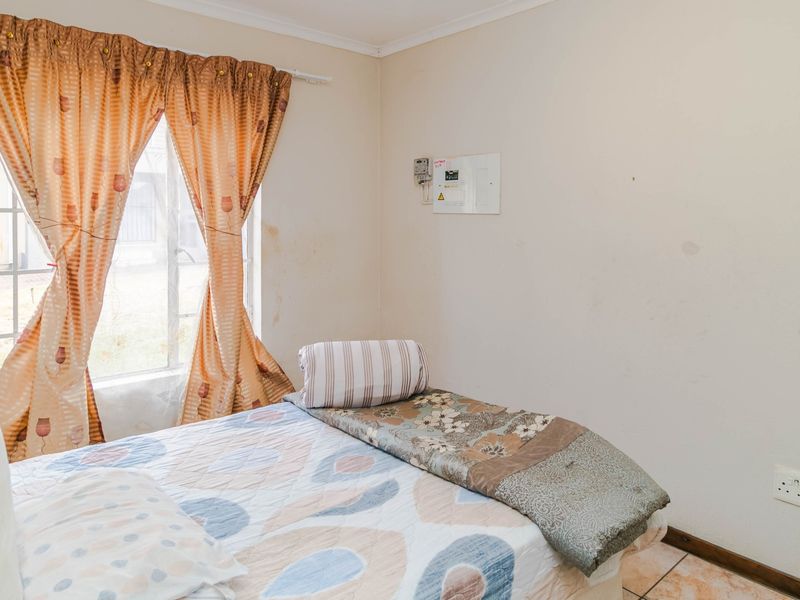 A bedroom featuring tiled flooring, a window with security bars, and a wall-mounted electrical distribution board.