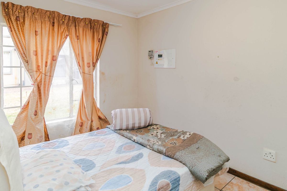 A bedroom featuring tiled flooring, a window with security bars, and a wall-mounted electrical distribution board.