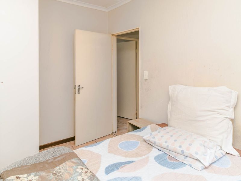 A bedroom featuring tiled flooring and a built-in wardrobe, showing signs of wear on the wall surfaces.