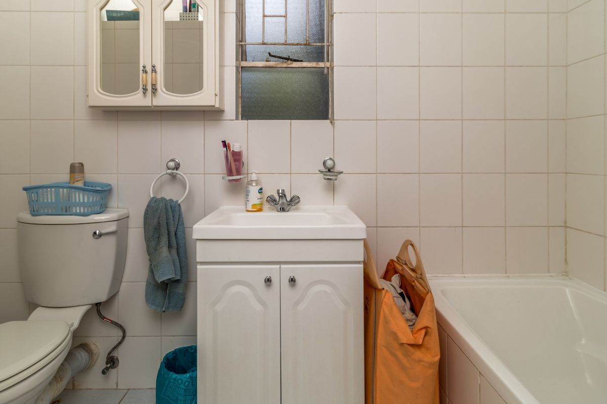 A functional bathroom featuring a standard bathtub, vanity cabinet with basin, and wall-to-wall tiling. The space would benefit from modern updates to fixtures and finishes.