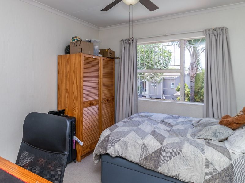 A functional bedroom featuring a ceiling fan, carpeted flooring, and a window fitted with security bars.
