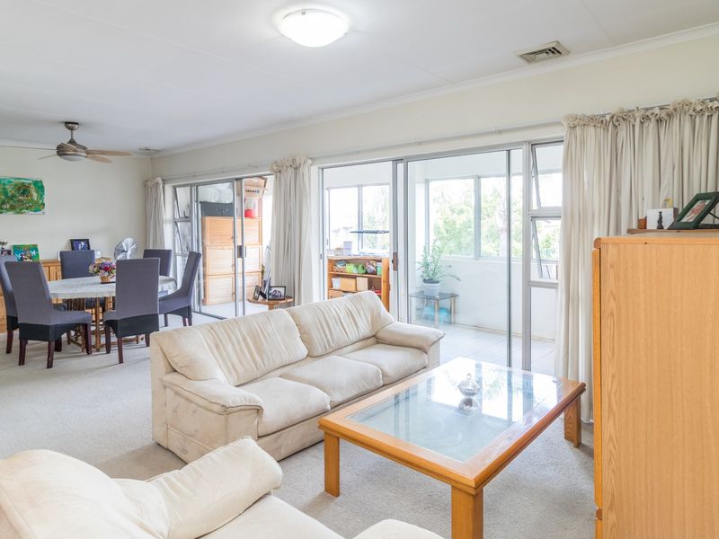 Spacious open-plan living and dining area featuring neutral carpeting, ceiling fan, and large sliding glass doors providing access to the balcony.