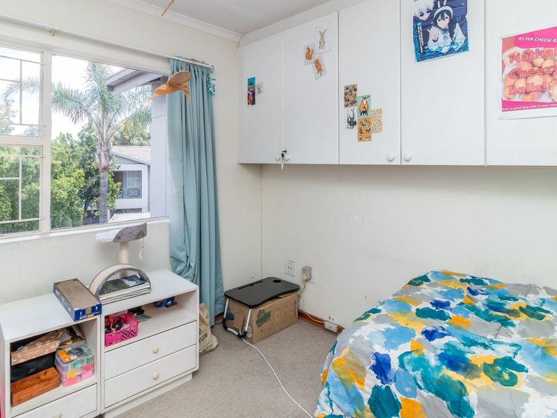 A bedroom featuring built-in cupboards, carpeted flooring, and a window with security bars, offering a functional space with potential for cosmetic updates.