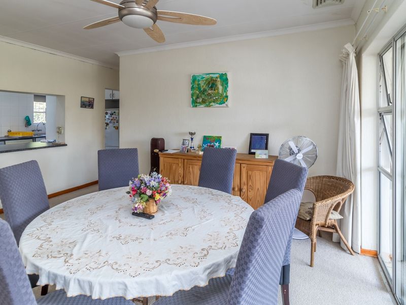 Open plan dining area featuring a ceiling fan, carpeted flooring, and a convenient pass-through window connecting to the kitchen space.