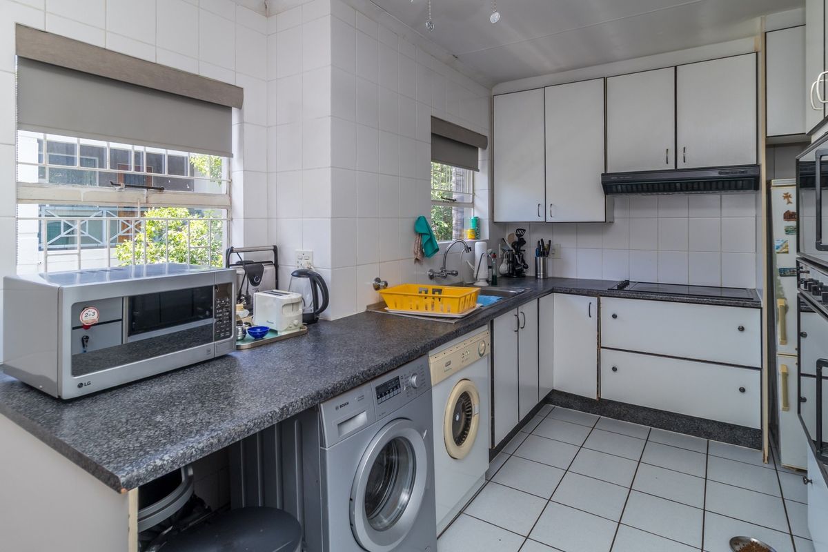 A functional kitchen featuring white cabinetry, dark laminate countertops, tiled backsplash, and integrated appliances, offering a practical layout with potential for modern updates.