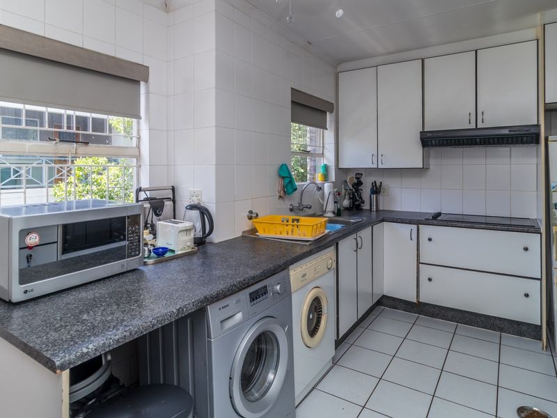 A functional kitchen featuring white cabinetry, dark laminate countertops, tiled backsplash, and integrated appliances, offering a practical layout with potential for modern updates.