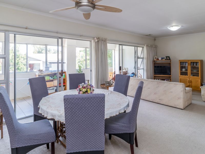 Spacious open-plan living and dining area featuring neutral carpeting, ceiling fan, and large sliding glass doors providing access to the balcony.