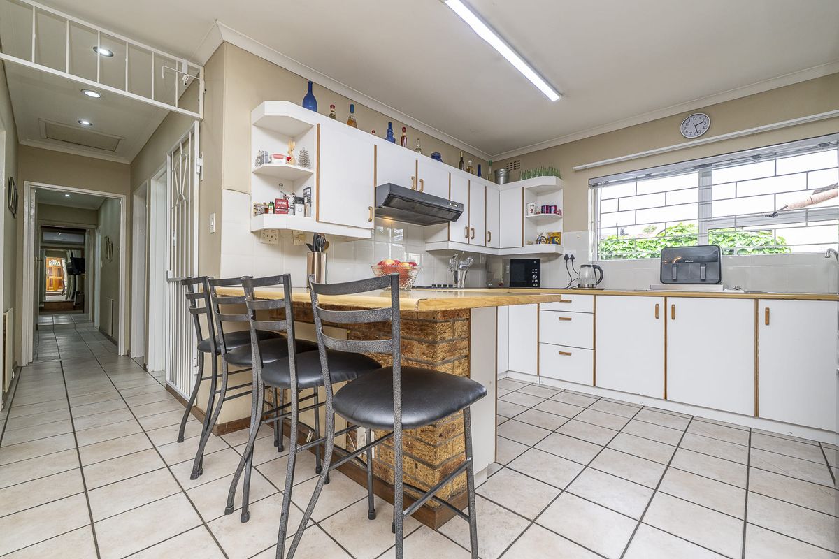 Functional kitchen featuring white cabinetry, a brick-based breakfast bar, tiled flooring, and a tiled backsplash with security bars on the window.