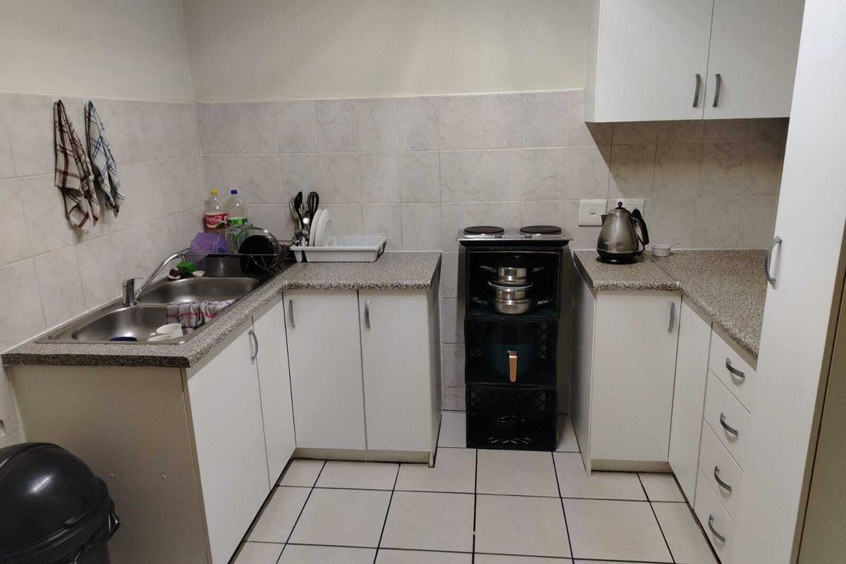 A compact kitchen featuring white cabinetry, laminate countertops, tiled backsplash, and ceramic floor tiles, providing a functional workspace with essential built-in fixtures.