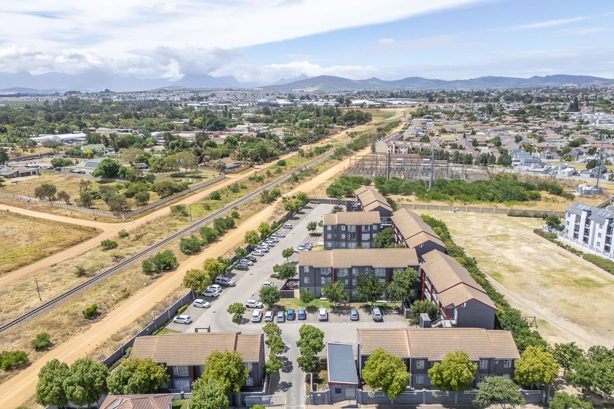 Aerial view of a residential apartment complex featuring multiple buildings, paved parking areas, and perimeter security walls within a suburban landscape.
