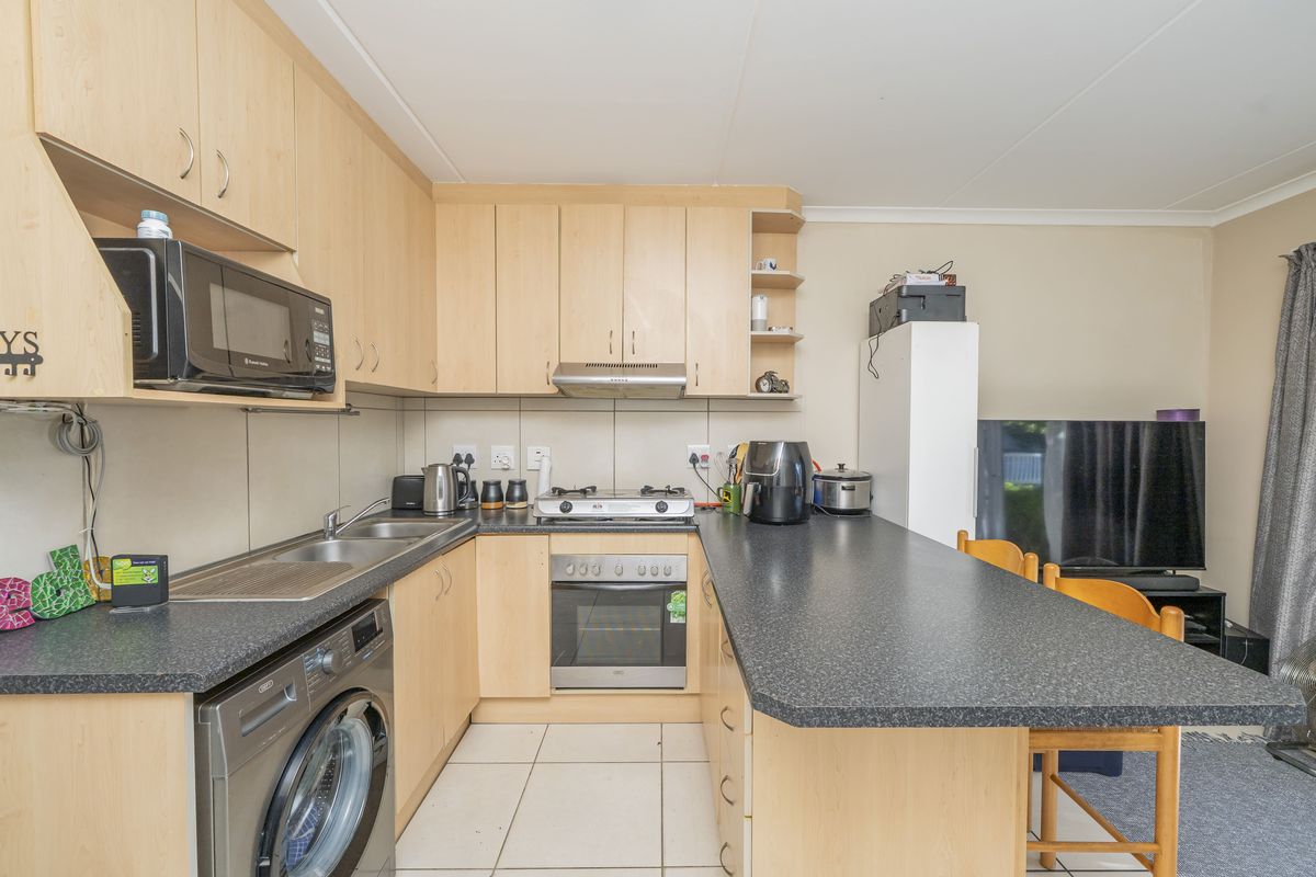 A functional kitchen featuring light wood-finish cabinetry, dark laminate countertops, a built-in oven with gas hob, and tiled flooring.