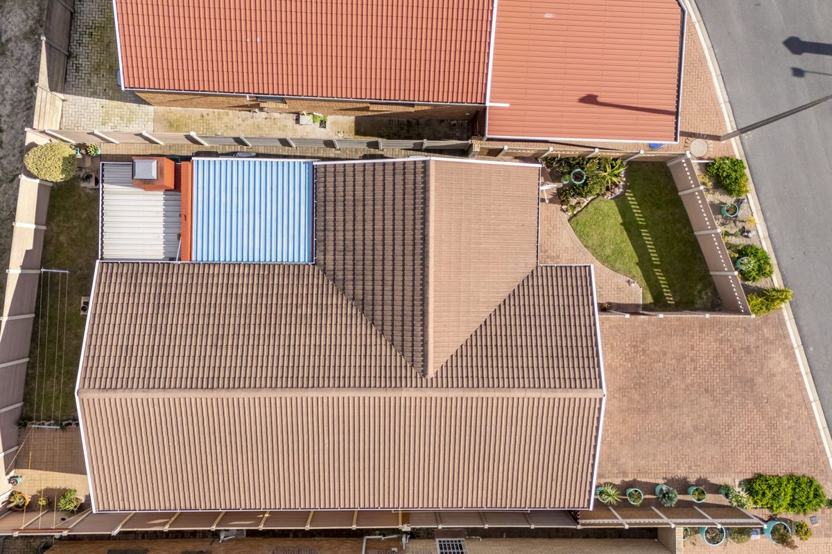 An aerial view of the property showing the tiled roof, paved driveway, surrounding boundary walls, and landscaped garden areas.