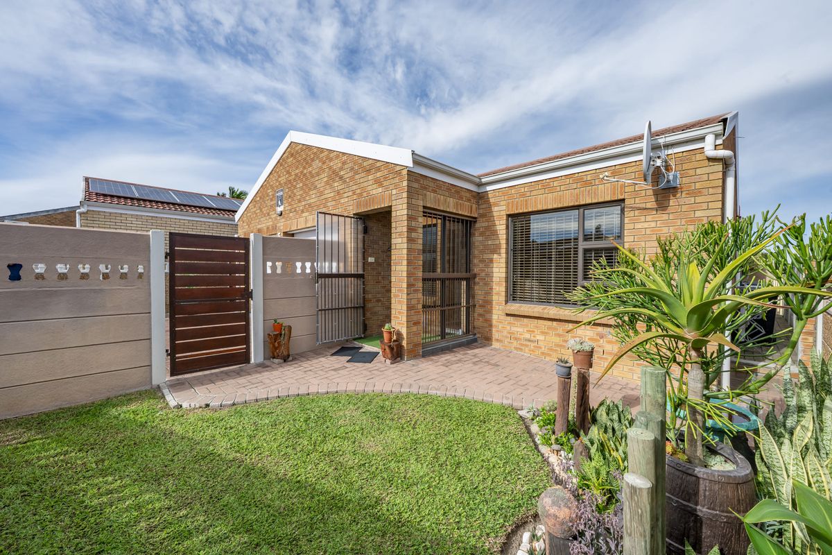 A well-maintained rear exterior view featuring a face brick facade, paved patio area, and a secure gated entrance with a small garden.