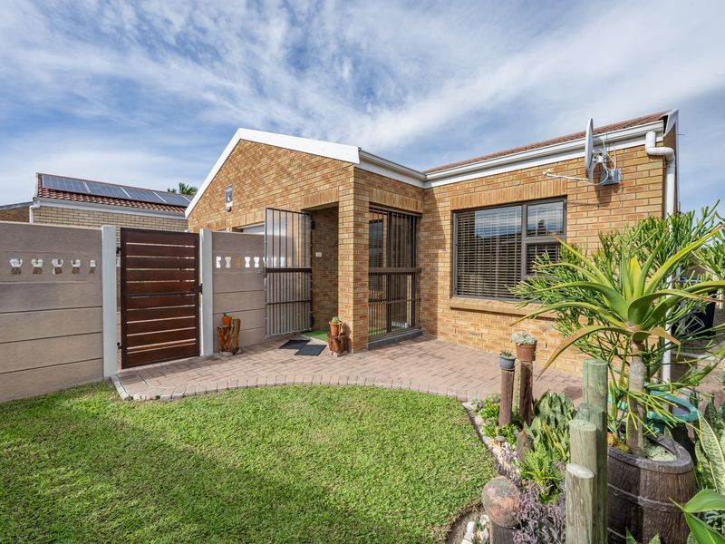A well-maintained rear exterior view featuring a face brick facade, paved patio area, and a secure gated entrance with a small garden.