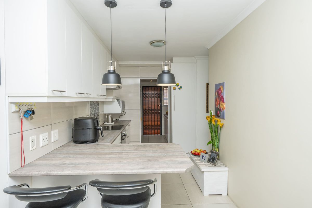 A modern, well-maintained kitchen featuring white cabinetry, a breakfast bar, tiled backsplash, and contemporary pendant lighting.